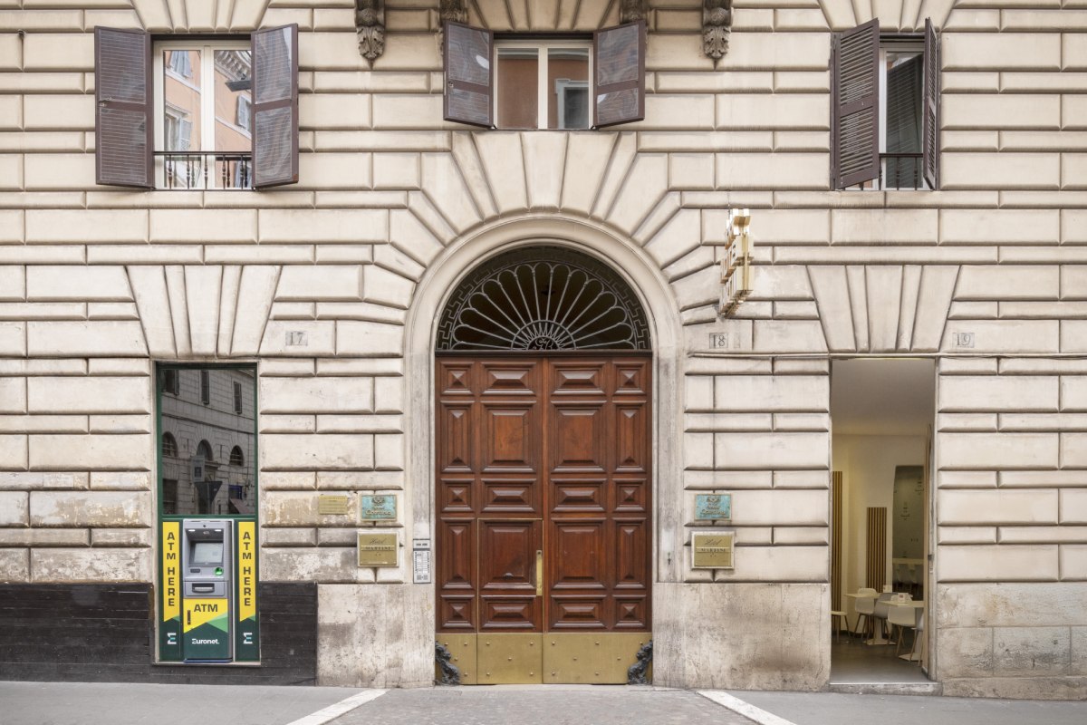Facciata esterna classica in pietra dell'Hotel Cortina a Roma, che mostra l'ingresso principale e un bancomat ATM Euronet - Hotel Cortina, BZAR hotels a Roma