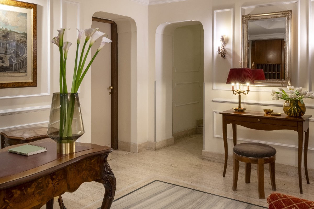 Vista interna della hall dell'Hotel Cortina a Roma, con archi aperti che mostrano lo spazio, pavimenti in marmo e una lampada d'epoca a tre luci - Hotel Cortina, BZAR hotels a Roma