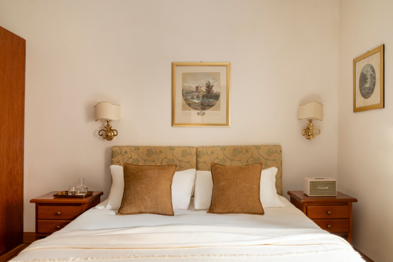 Dettaglio del letto matrimoniale in una camera standard dell'Hotel Cortina a Roma, con testata decorata, due cuscini in velluto marrone e due comodini d'epoca con lampade coordinate - Hotel Cortina, BZAR hotels a Roma
