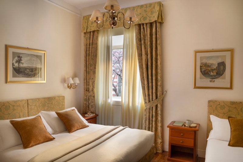 Ampia camera tripla dell'Hotel Cortina a Roma, composta da un letto matrimoniale e un letto singolo separato, arredata in stile classico con pavimenti in legno, quadri d'epoca e una luminosa finestra centrale - Hotel Cortina, BZAR hotels a Roma